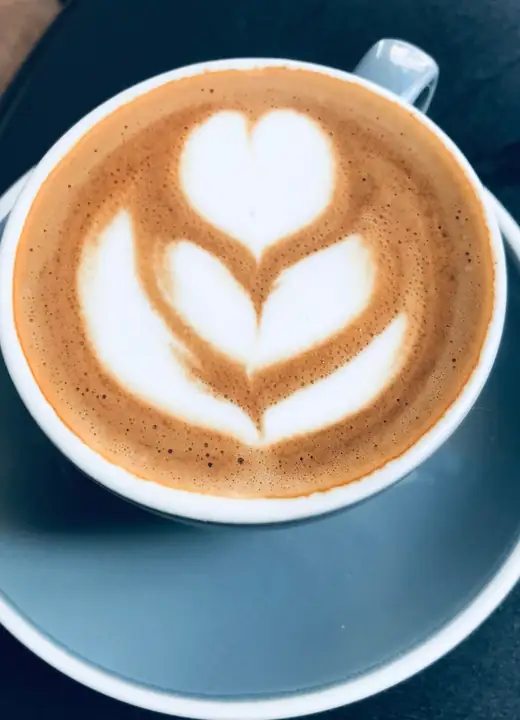 A flat white with heart latte art in a blue cup and saucer, seen from above