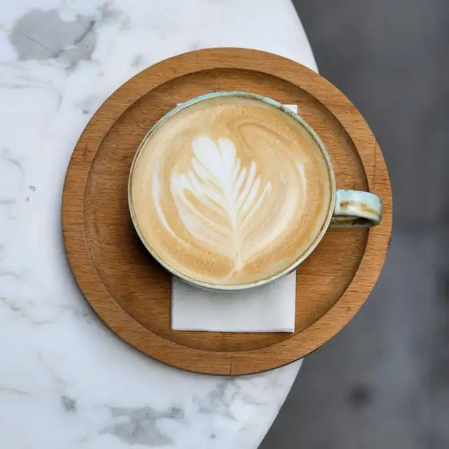 A cappuccino with latte art in a cup on a round wooden tray, on a marble table