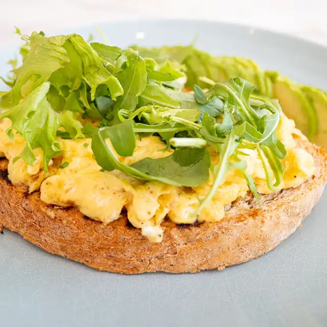 Scrambled eggs and avocado with green leaves on toasted sourdough